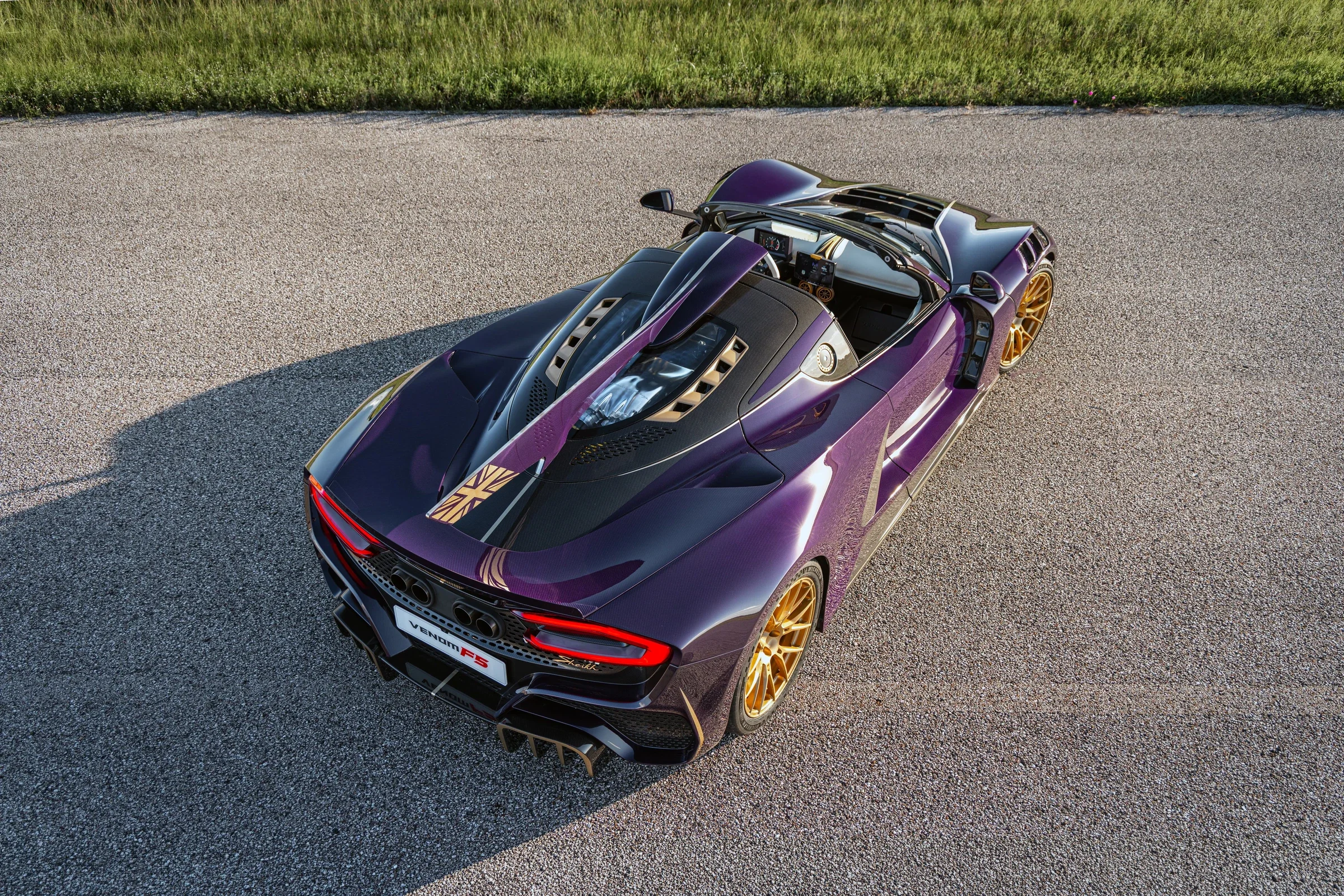 Violetter Hennessey Venom F5-M Roadster in erhöhter Heckansicht auf einer Landstraße